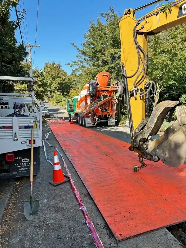 Backhoe lifting steel trench plate for concrete encasement of power conduit.